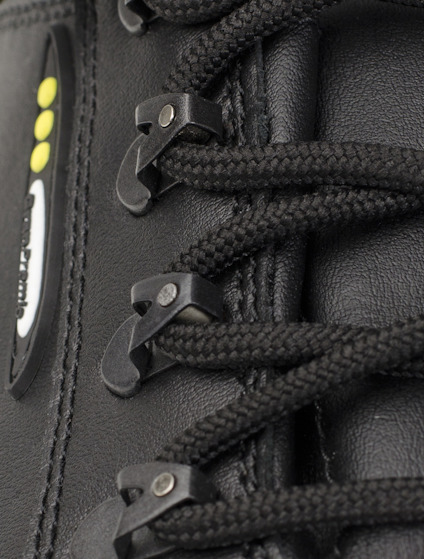 Svart stövel med svarta snören och hyskor. Del av en logotyp med tre gula prickar syns.