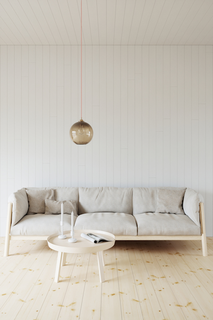 Beige soffa och runt bord på ljust trägolv; hängande lampa ovanför.