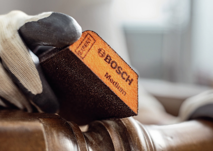 Hand i handske håller en Bosch medium slipblock mot en yta.