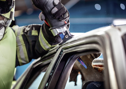 Brandman i skyddsutrustning använder ett verktyg för att skära i bilens kaross vid ett räddningsuppdrag.