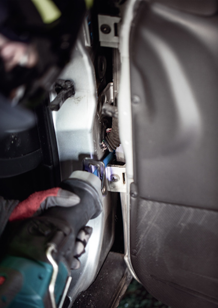 Person i skyddsutrustning använder ett verktyg för att manipulera en bilens dörrmekanism.