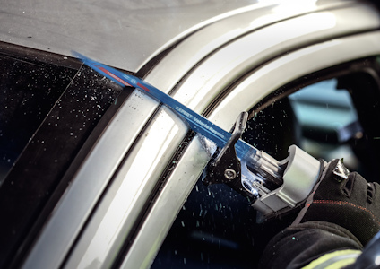 En person använder en såg för att skära genom en bilruta.