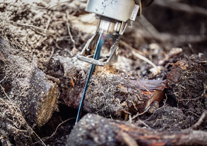 Motorsåg skär genom trä med bluaktigt sken runt bladet, omgiven av jord och bark.