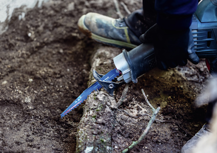 Person använder en blå motorsåg för att kapa en träbit nära marken.