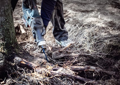 Person använder en motoriserad såg för att skära rötter nära ett träd.