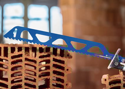 Blå såg med tandad klinga skär genom rött tegel i en byggnadsmiljö.