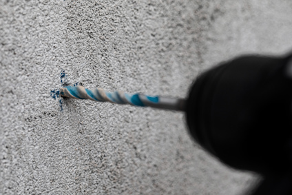 Borr skär in i betongvägg, med blå borrspån runt hålet.