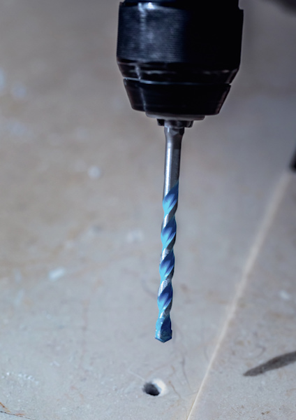 En borrmaskin med ett blått borrspets över ett litet hål i en beige yta.