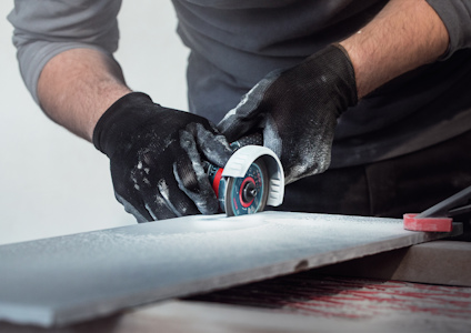 Person med svarta handskar slipar en skiva med ett litet slipverktyg på ett bord.