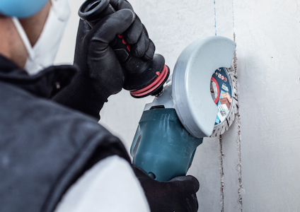 Person använder en vinkelslip med sliprondell på betongvägg.