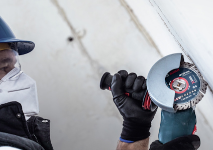 En person i skyddsutrustning använder en vinkelslip för att kapa en vit materialyta.