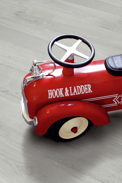 Röd leksaksbrandbil med texten "HOOK & LADDER" på sidan, står på ett trägolv.