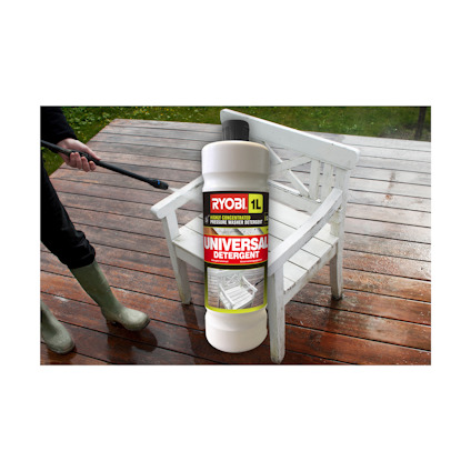 Vit plastflaska med etikett "RYOBI Universal Detergent" hålls framför en vit trädgårdsbänk. Person i gröna stövlar syns.