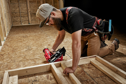 En person med verktygsbälte bygger en träram på ett golv av OSB-skivor.