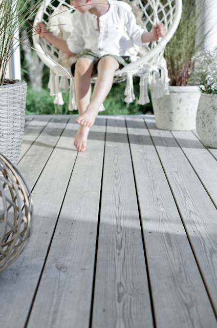 Trätrall med flera krukor och en hängande stol med ett barn i vit klädsel.