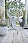Hängstol med en randig filt på en träveranda med krukväxter och en svart dekorationslampa.