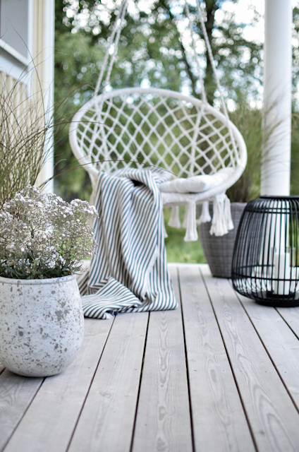 Hängstol med en randig filt på en träveranda med krukväxter och en svart dekorationslampa.