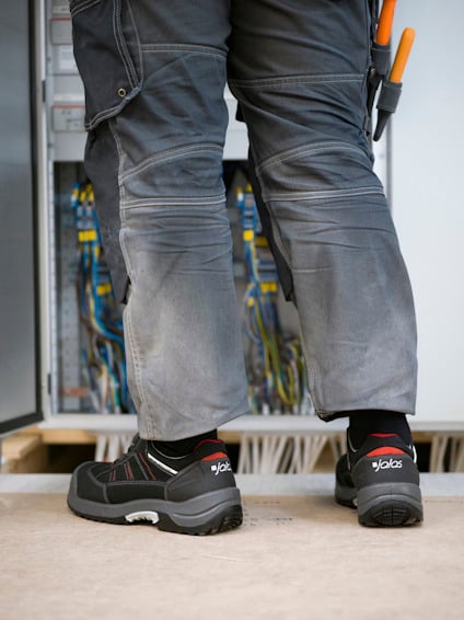 Person i arbetskläder står framför ett öppet elskåp med kablar.