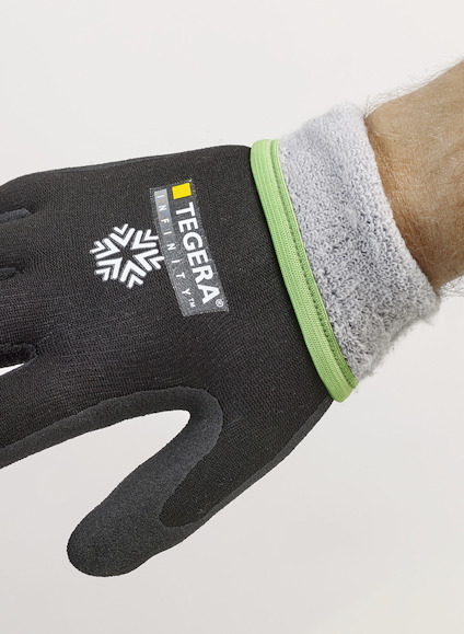 Svart handske med grå insida och grönt kantband, märkt "TEGERA", på en persons hand.
