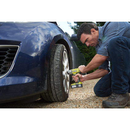 Person använder en grön och svart batteridriven skruvdragare för att byta däck på en bil.