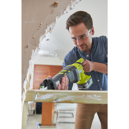 En person använder en grön och svart batteridriven tigersåg för att såga trä inomhus.