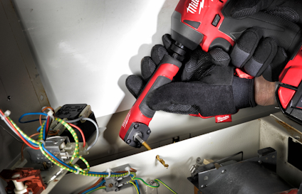 Hand med svarta handskar håller i en röd elektrisk verktyg nära öppna kablar och komponenter.