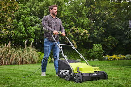 En person använder en grön RYOBI gräsmattaresare på en gräsmatta med träd och buskar i bakgrunden.