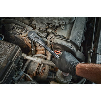 En person med svarta handskar använder en spärrnyckel på en motor i en bil.