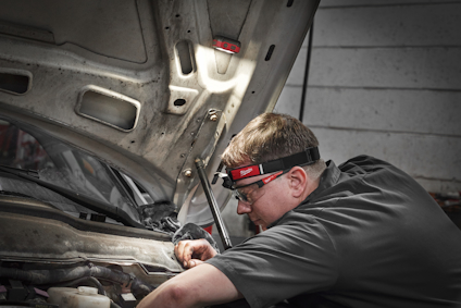 En person arbetar under en bilmotorhuv med en pannlampa på huvudet.