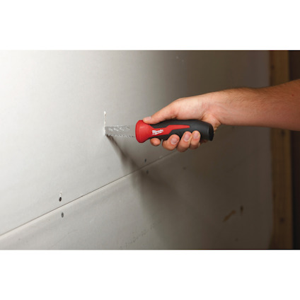 Hand som håller en såg mot en gipsskiva vägg.