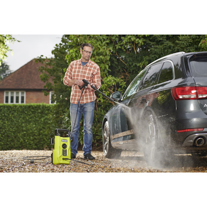 Man tvättar svart bil med högtryckstvätt utomhus.