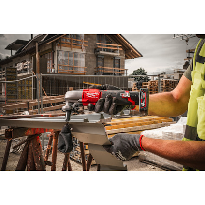 En person använder en röd elverktyg på en metallplåt vid en byggarbetsplats.