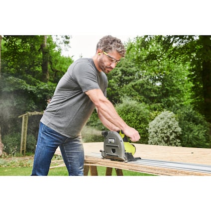 Man som använder en grön och svart cirkelsåg på en träskiva utomhus.