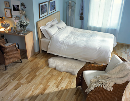 Sovrum med trägolv, en stor dubbelsäng, rottingstolar och flera tavlor på väggarna.