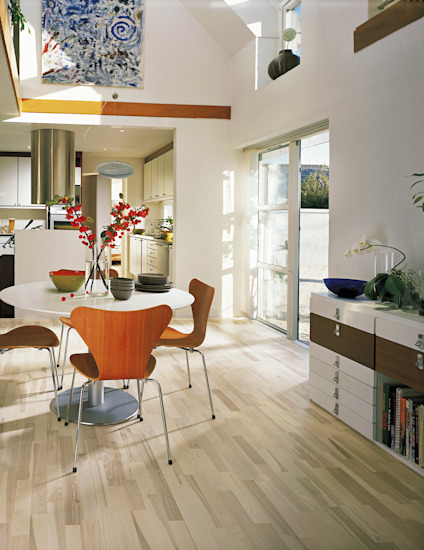 Modernt kök med trästolar, runt bord, växter och stort fönster. Ljusa trä- och vita ytor.