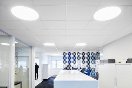 Modernt kontorsutrymme med vita takpaneler och stora, runda ljuskällor.