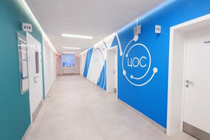 En korridor med vita dörrar och färgglada väggar i grönt och blått, samt texten "ЦОС" på väggen.