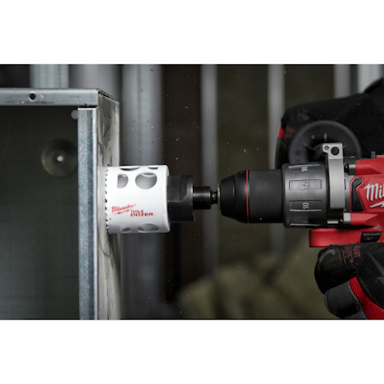 En person borrar med en röd borrmaskin, vars borr är märkt "Milwaukee 102 mm".