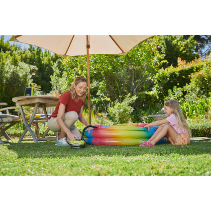 Kvinna och barn leker med en uppblåsbar pool i trädgården. Multikompressor från Ryobi syns i bild.