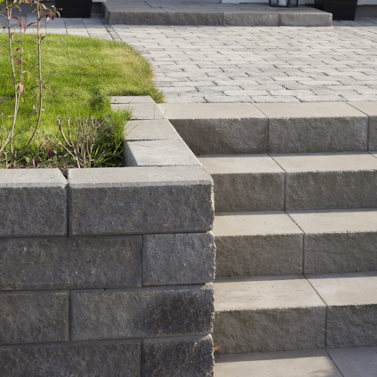 Trappsteg av betongsten, omgiven av stödmur av liknande sten och en sektion med gräsmatta.