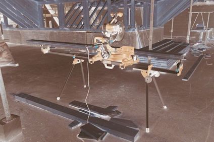 Kap- och geringssåg på ett stativ i en byggnad med synliga träbjälkar och plankor på golvet.