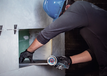 Person med blå hjälm använder en vinkelslip för att såga gipsvägg.