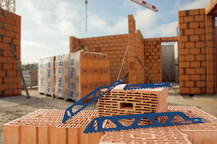 Röda tegelstenar staplade på en byggarbetsplats med murar under uppbyggnad i bakgrunden.