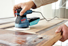 Person slipar trädörr med en blå och svart Bosch excenterslipmaskin.
