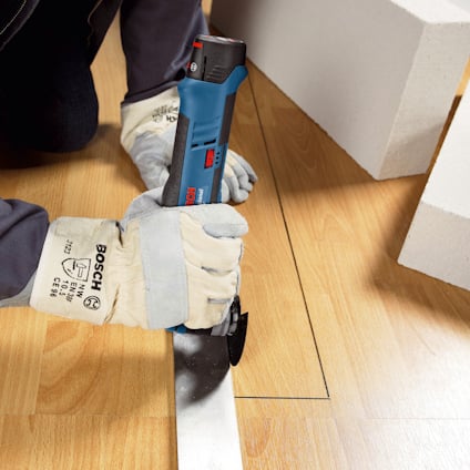 Person i skyddshandskar använder en Bosch elverktyg för att skära i ett laminatgolv.