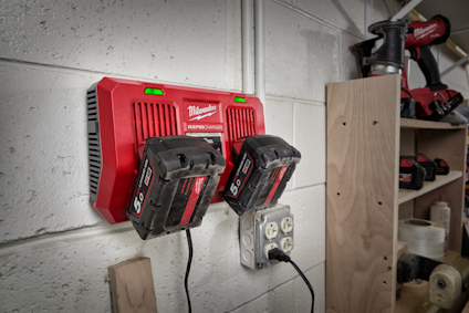 Laddningsstation med två Milwaukee 5.0Ah batterier monterad på en vit vägg, kopplad till ett eluttag.