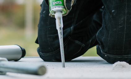 Person på huk applicerar ankarmassa i ett borrhål utomhus. Verktyg ligger bredvid.