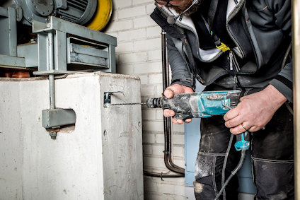 Person som använder en blå borrmaskin för att borra i en betongvägg bredvid industriell utrustning.