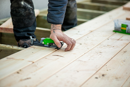 En person använder ett grönt och svart verktyg för dolt montage när trallbrädor monteras utomhus.