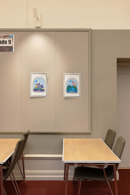 Två affischer med ryggsäckar på en vägg ovanför bord och stolar. Texten "Grade 9" syns delvis.